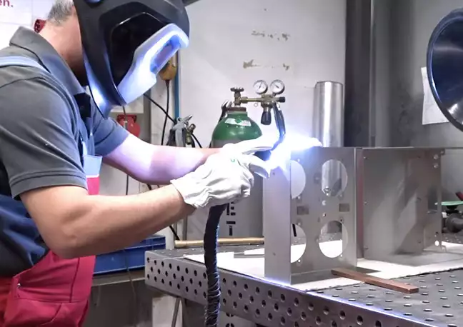 Headerbild für Webseite Prozesse Schweißen: Mitarbeiter schweißt Elemente für eine Baugruppe von Hand.